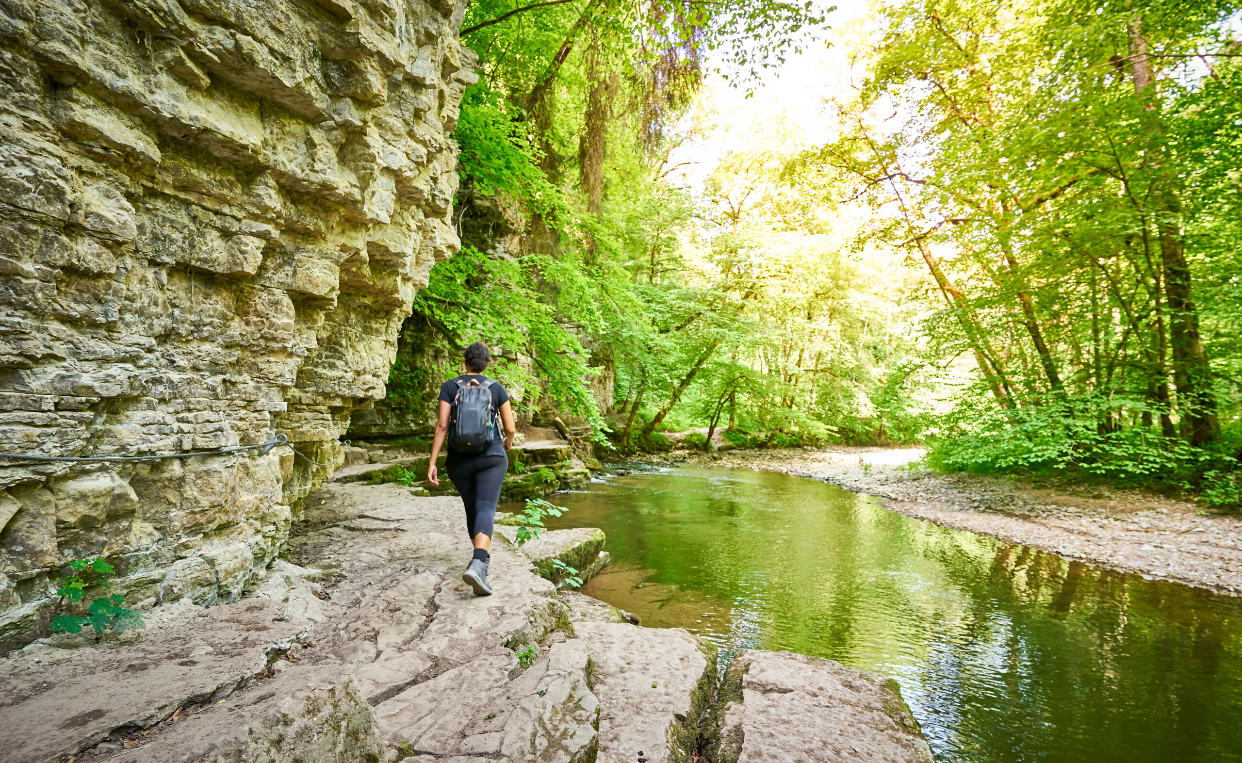 Ein Frau die in der Wutachschlucht direkt neben dem Fluss durch den Wald wandert.