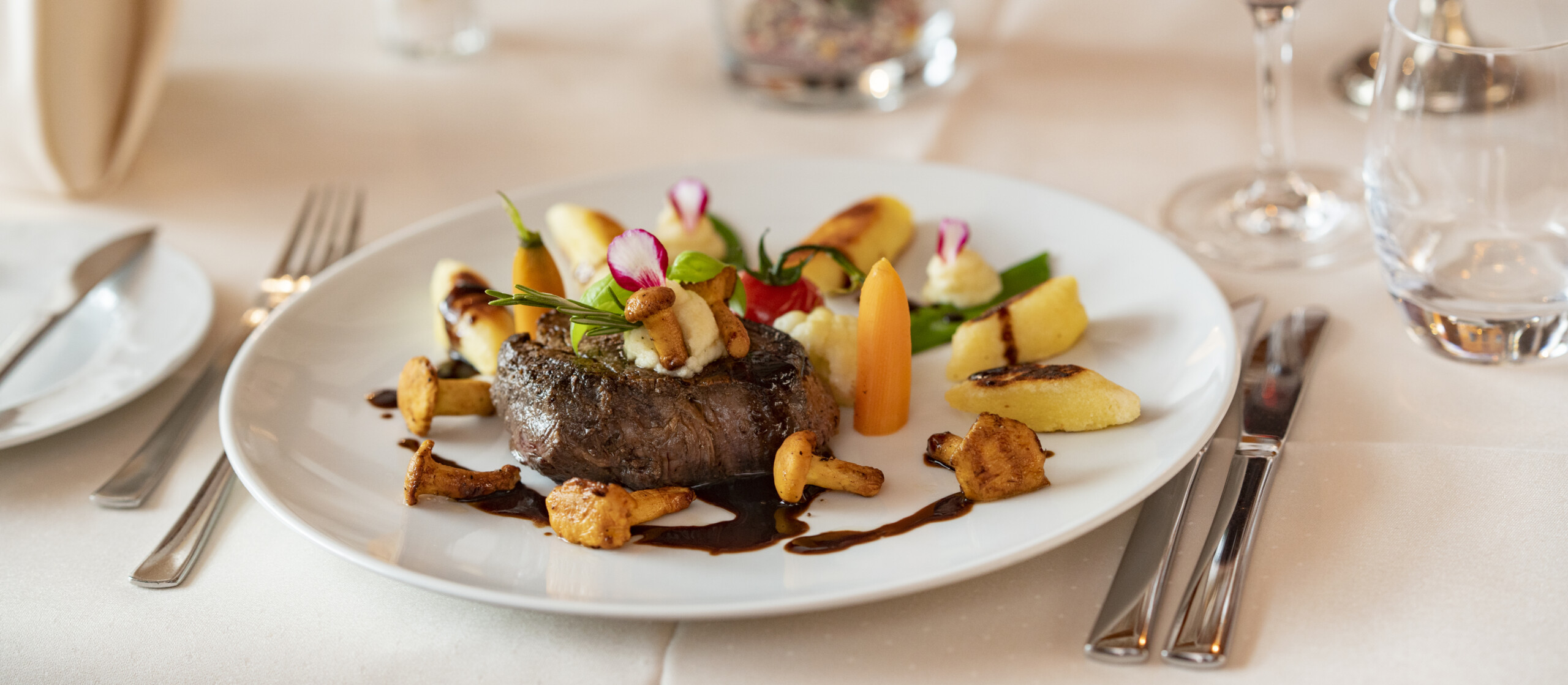 Teller mit Steak, Pfifferlingen, Karotten und Kartoffeln auf einem schön gedeckten Tisch.