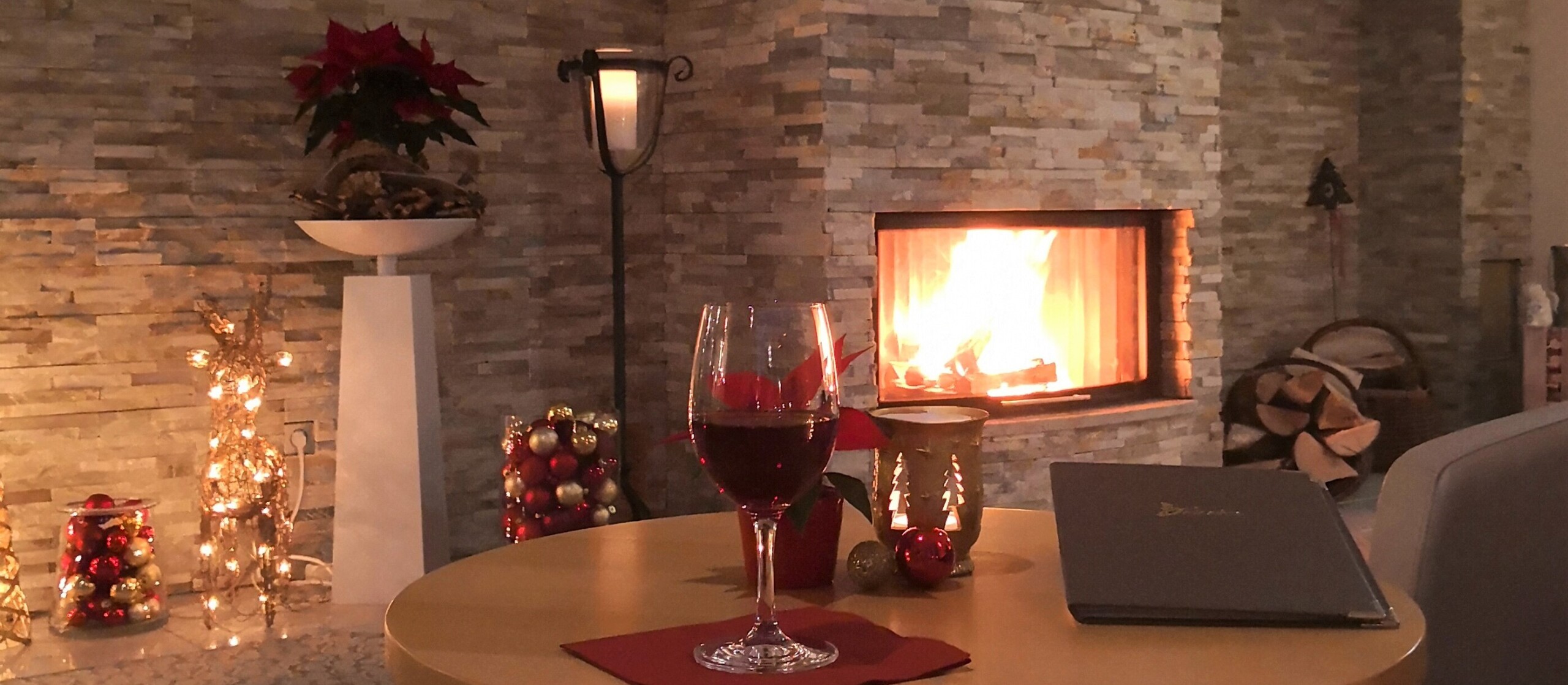 Tisch mit Weihnachtsdeko und Weinglas vor einem Kamin.