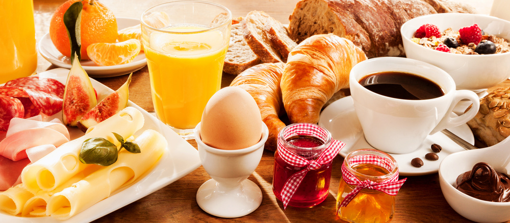 Frühstück mit Kaffee, Orangensaft, Brot, Croissants, Müsli,, Ei, Marmelade, Wurst und Käse.