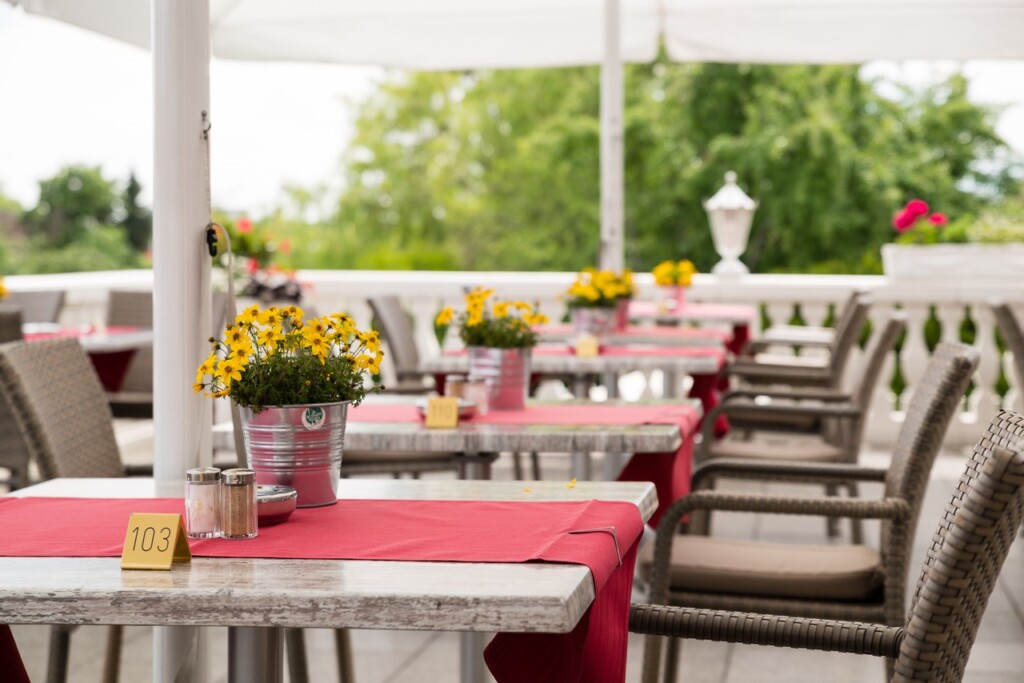 Terrasse im Sommer mit Tischen mit gelben Blumen und roter Tischdecke.