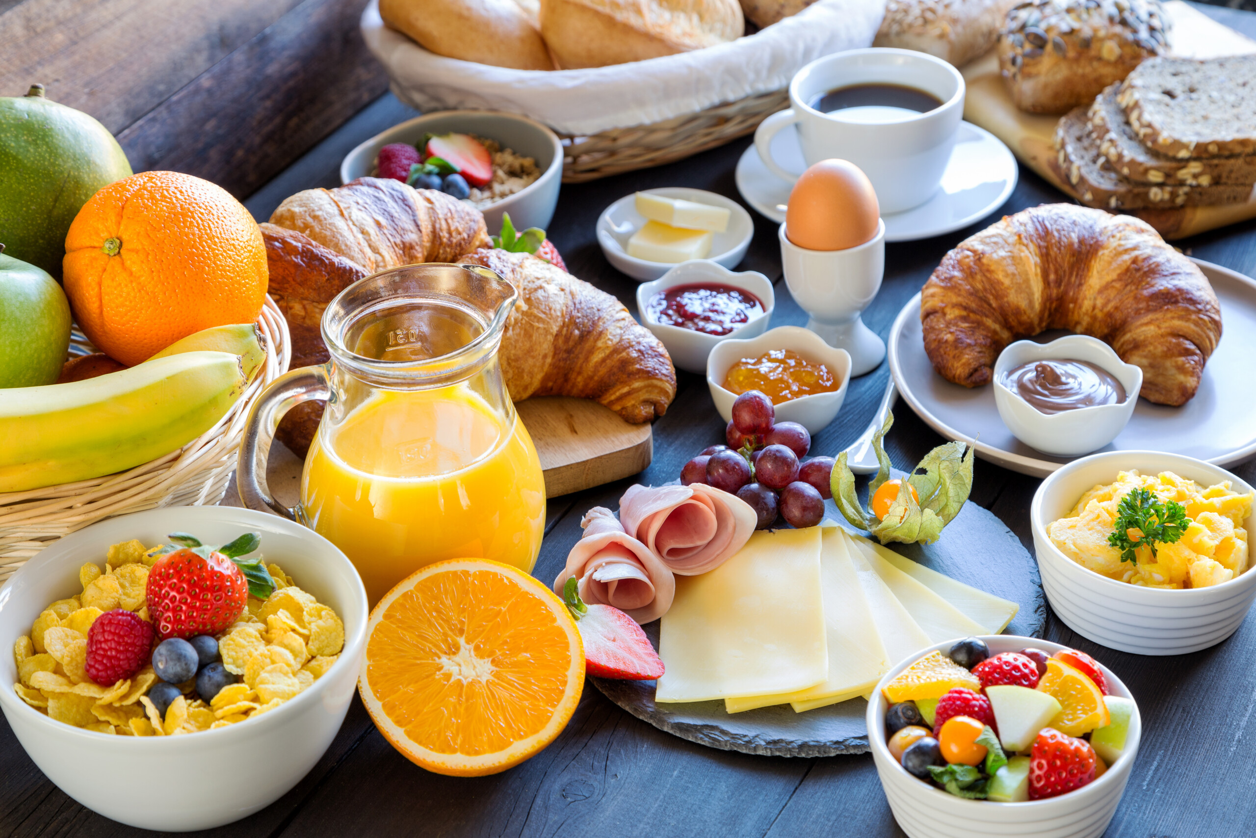 Frühstück mit Kaffee, Orangensaft, Brot, Croissants, Müsli,, Ei, Marmelade, Wurst und Käse.