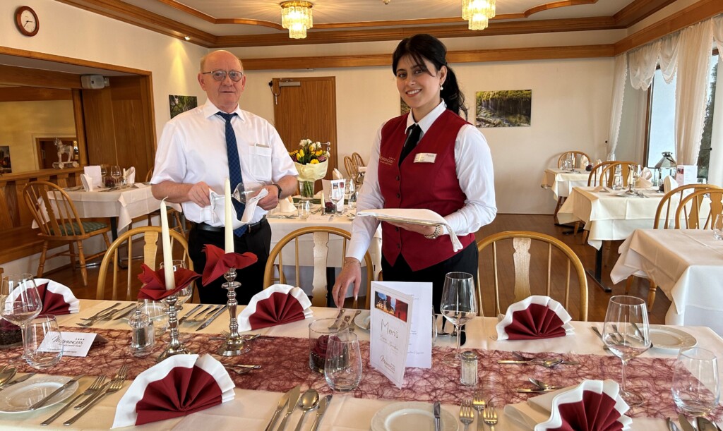 Eine Auszubildende und der Restaurantleiter decken gemeinsam einen Tisch im Restaurant ein.